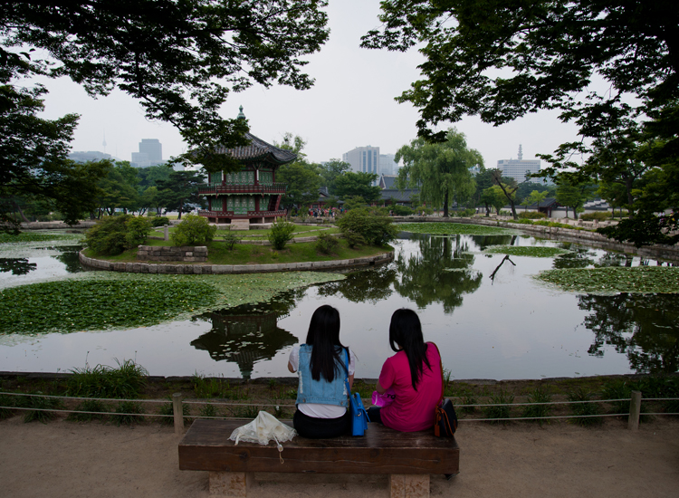 due turiste riposano sul bordo del lago che fronteggia Palazzo Gyeongbokgung due turiste riposano sul bordo del lago che fronteggia Palazzo Gyeongbokgung